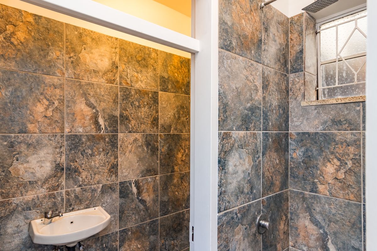 A compact bathroom featuring full-height stone-look wall tiling, a wall-mounted basin, and a shower area with a small window.