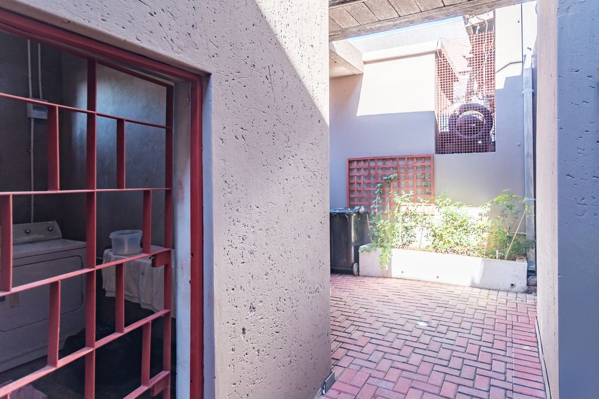 A functional outdoor courtyard area featuring brick paving, a raised planter box, and a secure utility room access point.
