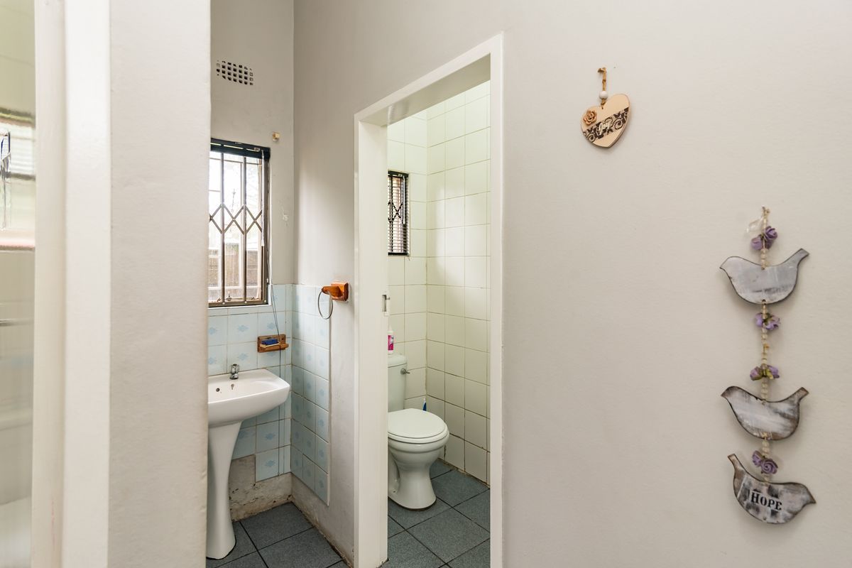 A functional bathroom featuring a pedestal basin and a separate toilet cubicle with tiled walls and flooring.