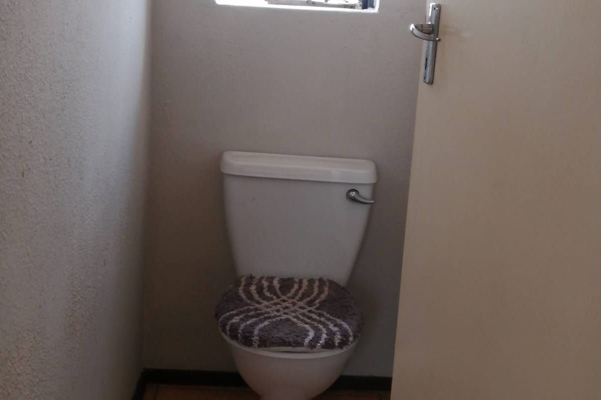 A compact guest toilet featuring ceramic floor tiles, a standard white toilet suite, and a window with security bars.