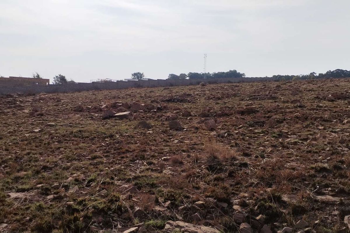 A wide-angle view of a vacant residential plot featuring natural rocky terrain and perimeter boundary walling in the distance.