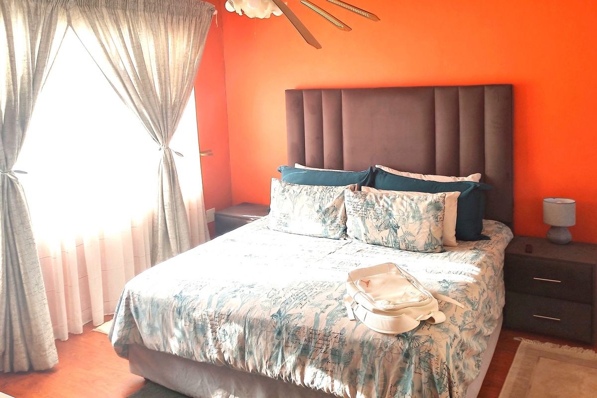 A bedroom featuring bright orange walls, a ceiling fan, and large windows with curtains.