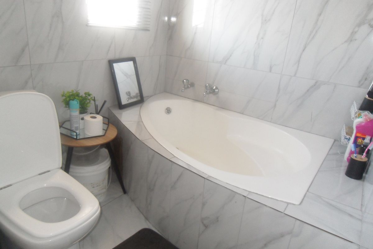 A modern bathroom featuring marble-look wall and floor tiles, a built-in bathtub with chrome fixtures, and a standard toilet.