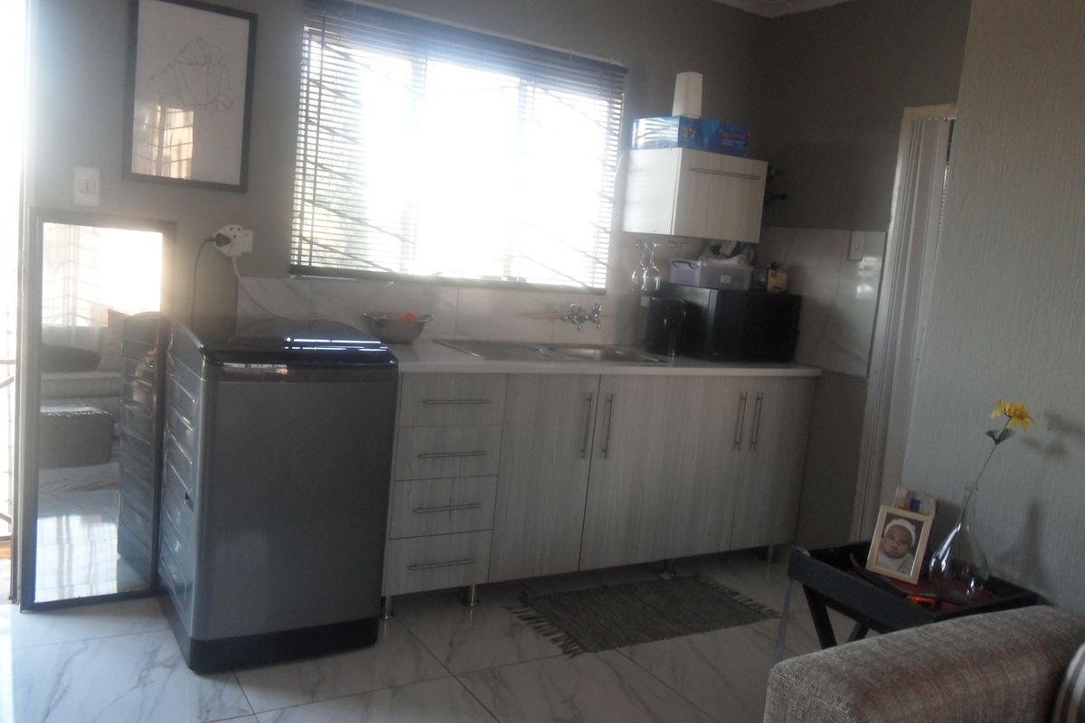 A functional kitchen area featuring light wood-grain cabinetry, a stainless steel sink, and tiled flooring, illuminated by natural light from the window.