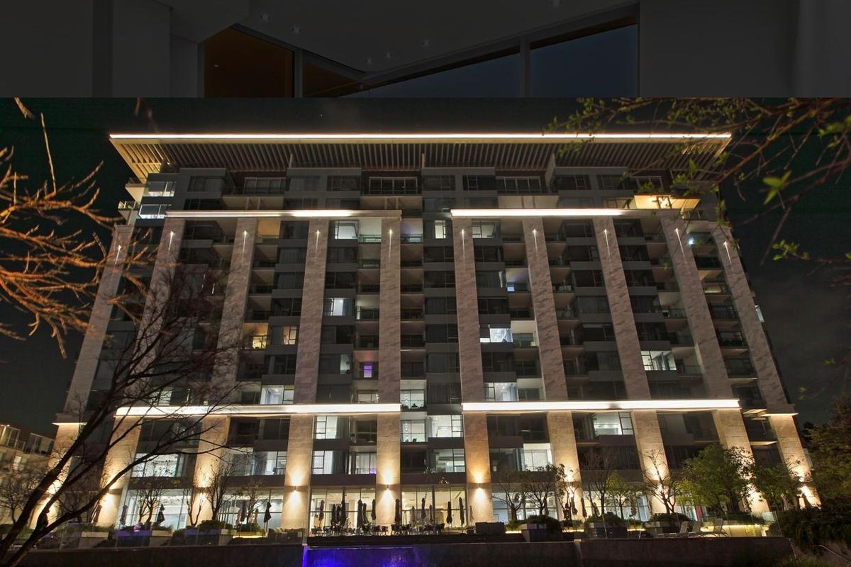 A striking night view of a modern apartment building facade featuring architectural lighting, balconies, and landscaped grounds.