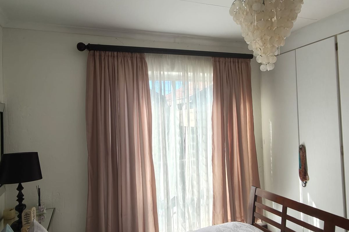 A bedroom featuring built-in cupboards, a window with curtain tracks, and a decorative ceiling light fixture.