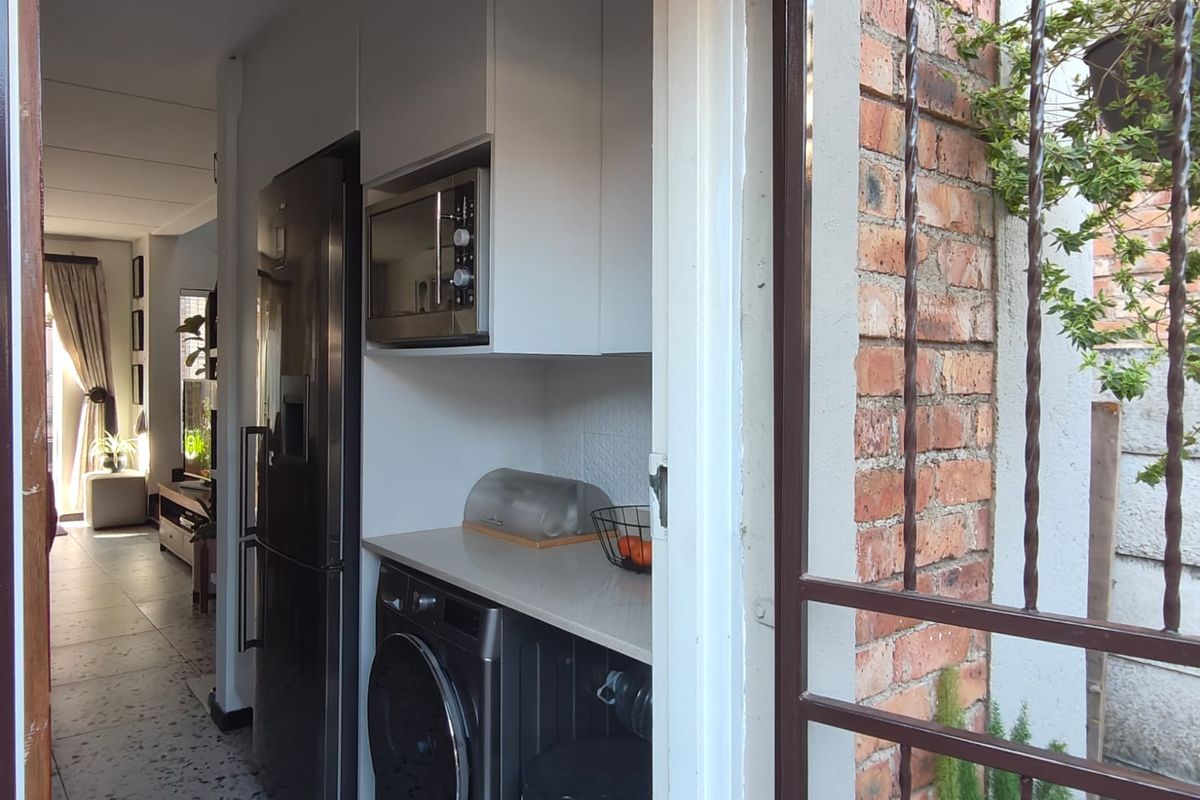 A compact kitchen area featuring built-in cabinetry, a microwave, and space for laundry appliances, with direct access to an outdoor area.
