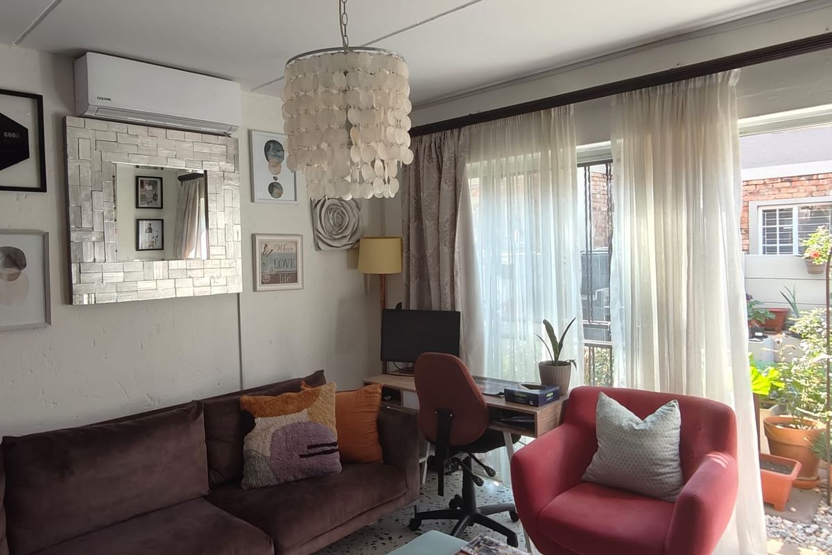 A bright living room featuring a wall-mounted air conditioning unit, terrazzo flooring, and large sliding glass doors providing access to an outdoor patio area.