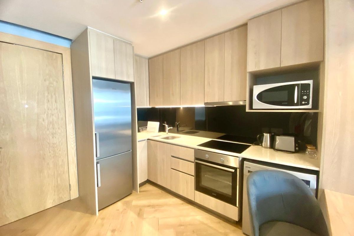 Modern kitchen featuring light wood cabinetry, integrated stainless steel appliances, a sleek black glass splashback, and light-toned herringbone flooring.