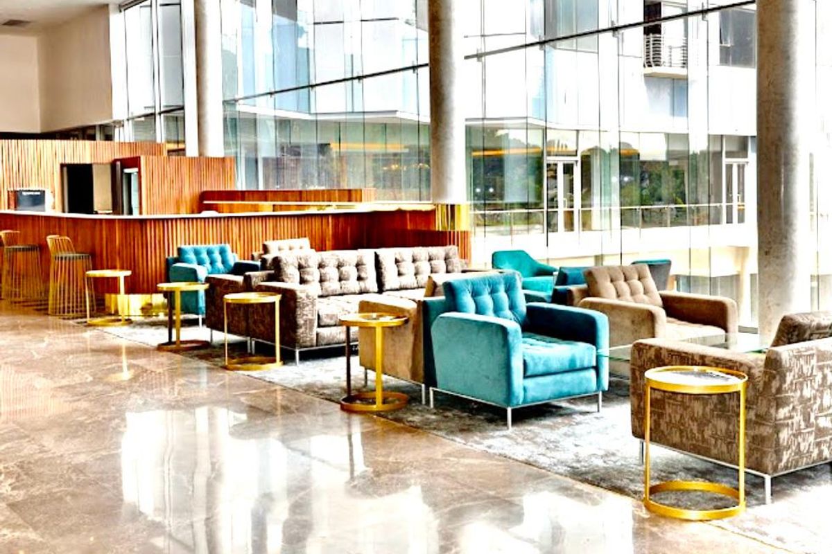 Spacious modern lounge area featuring floor-to-ceiling glass windows, polished marble flooring, and a built-in bar counter with timber slat detailing.