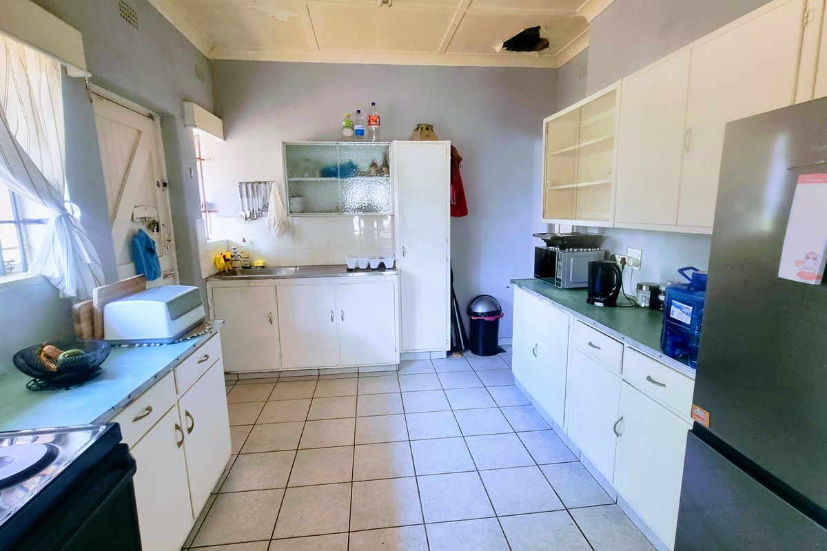 A dated kitchen featuring white cabinetry, tiled flooring, and a functional layout, currently showing signs of wear and ceiling damage.