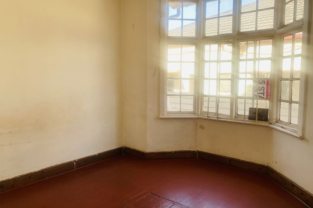 An empty room featuring a large bay window with timber frames and original painted wooden flooring, offering a blank canvas for renovation.
