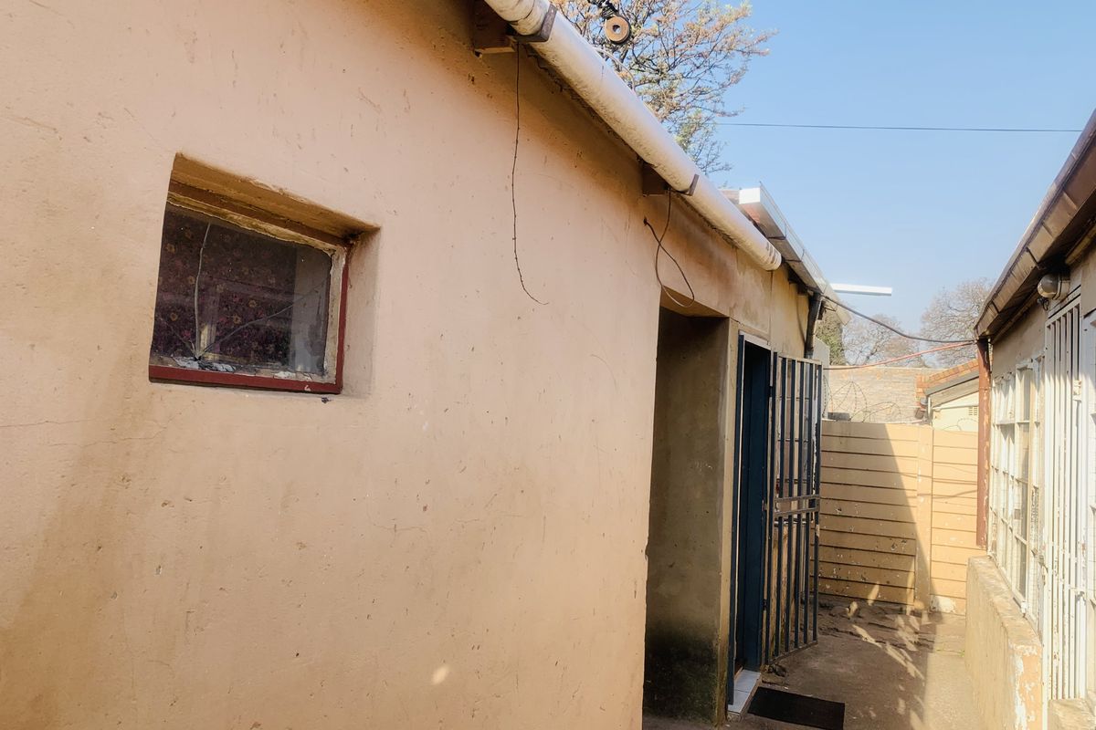 Exterior view of the side of the house showing a narrow walkway, security gate, and weathered wall finishes.