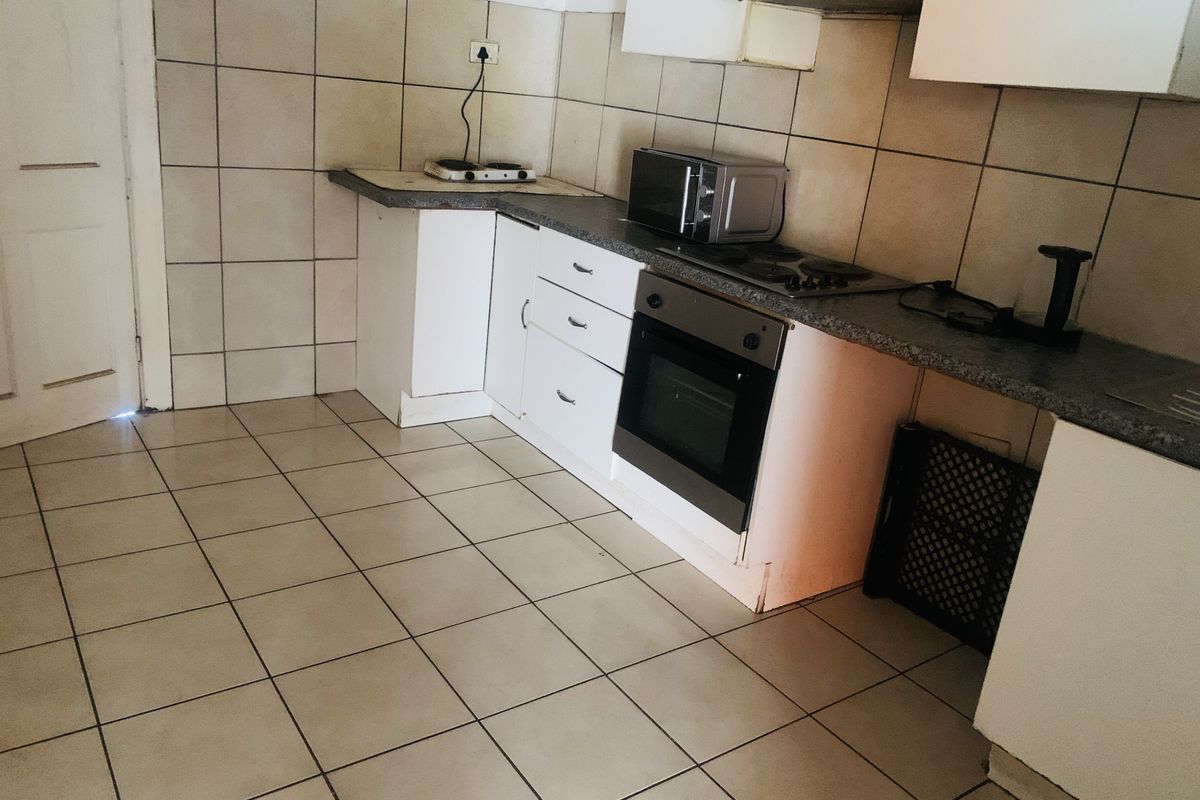 A functional kitchen featuring tiled flooring, wall-mounted cabinetry, a built-in oven, and a hob with an extractor fan.