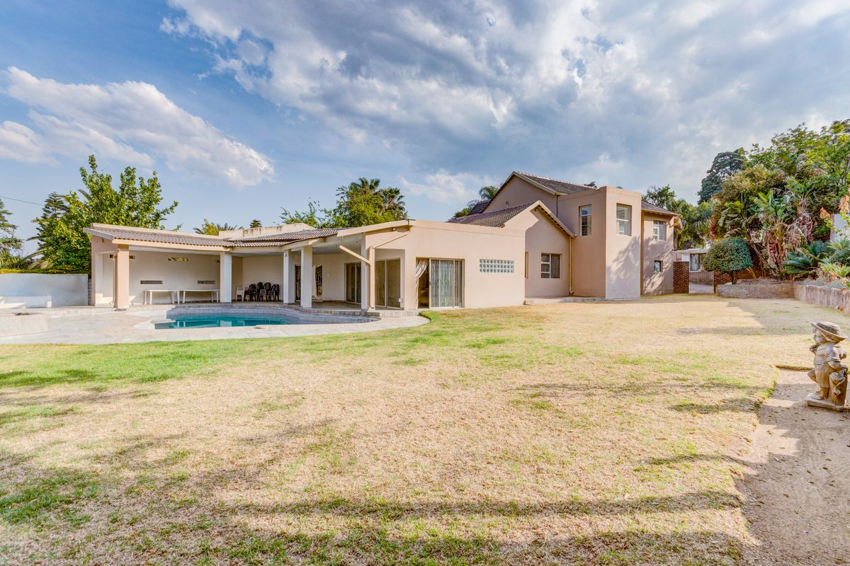 Spacious rear exterior view featuring a large lawn, a swimming pool, and a covered patio area attached to the main house structure.