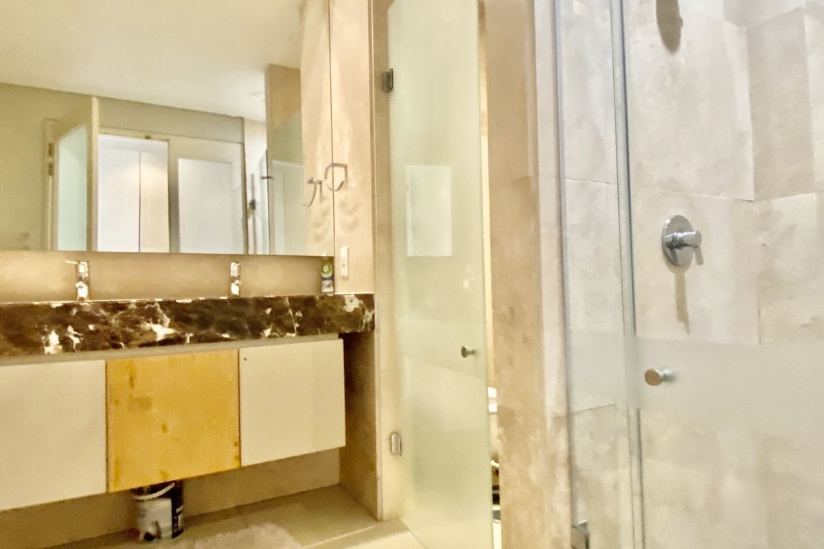A bathroom featuring a marble-topped vanity with dual basins, a large wall mirror, and a glass-enclosed shower area with stone tiling.