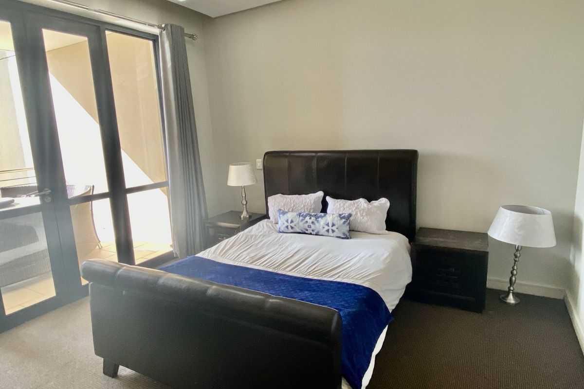 A bedroom featuring neutral walls, dark carpeting, and large glass sliding doors providing access to an outdoor balcony area.