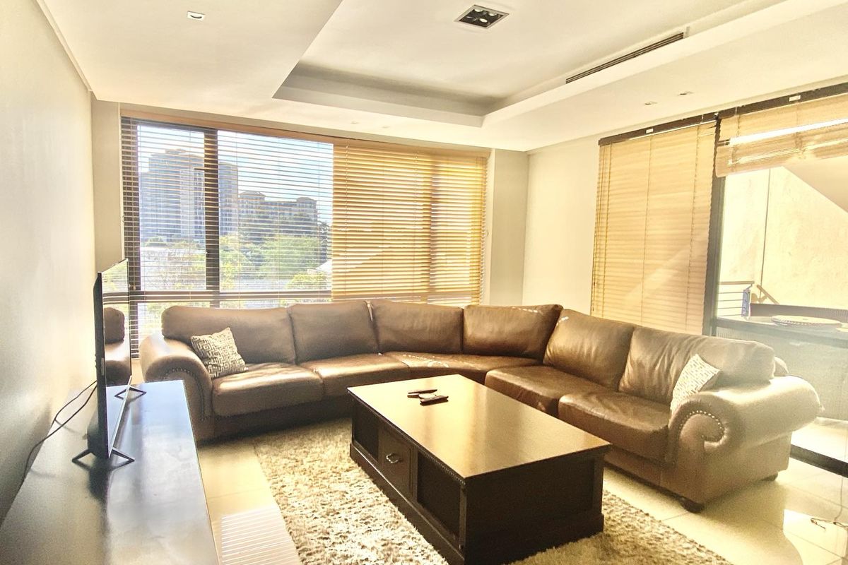 A bright and spacious living room featuring large windows with wooden blinds, recessed ceiling lighting, and tiled flooring.
