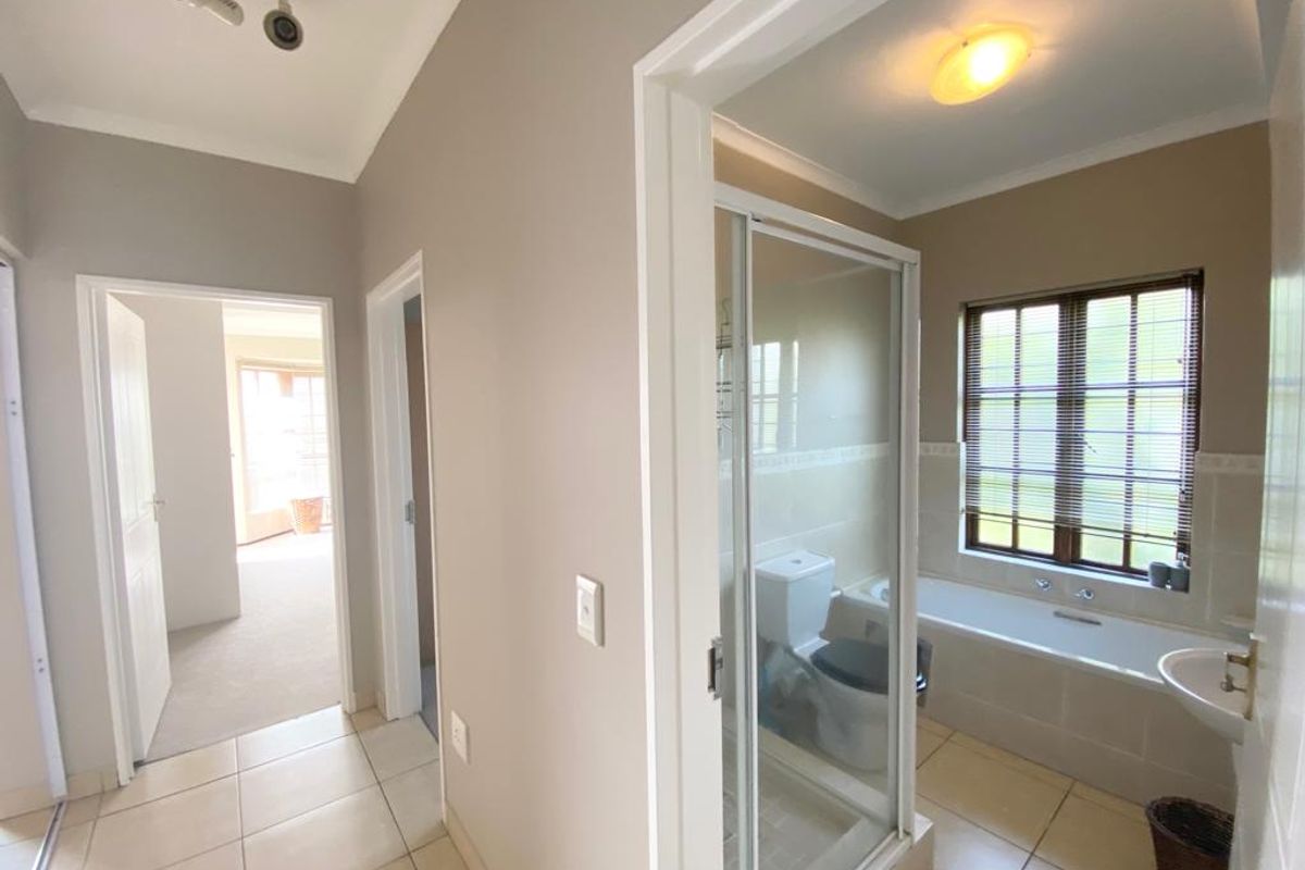 A view from the hallway into a functional bathroom featuring a separate shower, bathtub, and tiled flooring, with an adjacent bedroom visible.