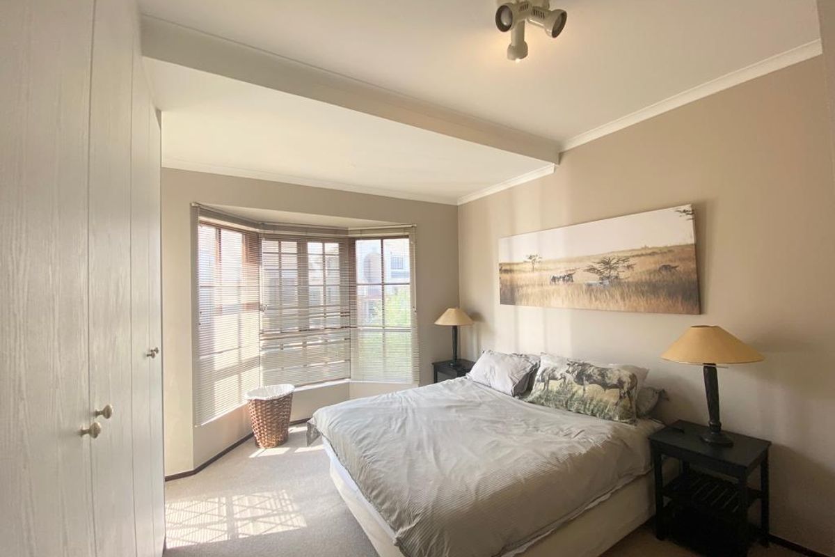A well-lit bedroom featuring built-in cupboards, neutral carpeting, and a large bay window that allows for ample natural light.