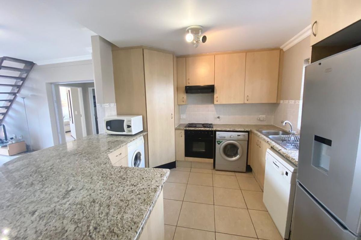 Functional kitchen featuring granite countertops, built-in oven, hob, extractor fan, and integrated space for laundry appliances, flowing into an open-plan living area.