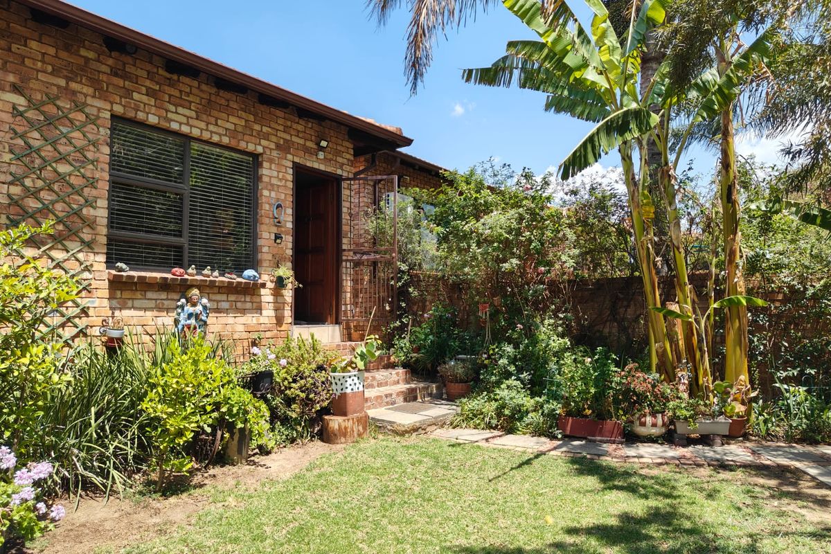A rear view of the townhouse featuring a face-brick facade, established garden with mature trees, and a paved entrance step.