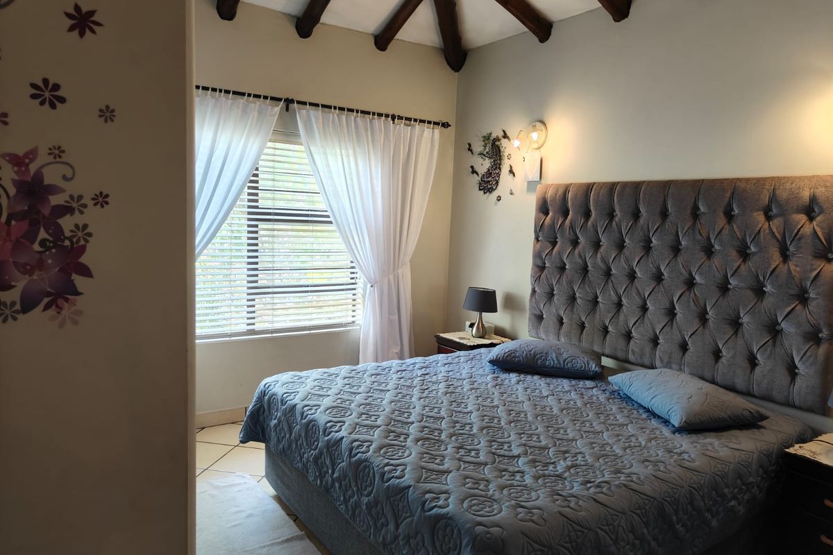 A bedroom featuring exposed timber ceiling beams, tiled flooring, and a window with fitted blinds.