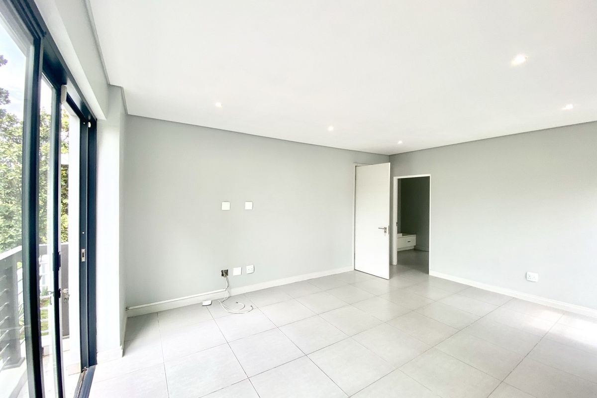 A bright, empty living room featuring large sliding glass doors, neutral tiled flooring, recessed ceiling lighting, and a clean, modern aesthetic.