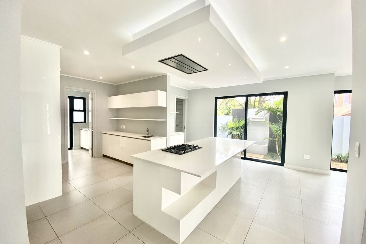 Modern open-plan kitchen featuring a central island with a built-in gas hob, sleek cabinetry, recessed ceiling lighting, and large sliding doors to the garden.