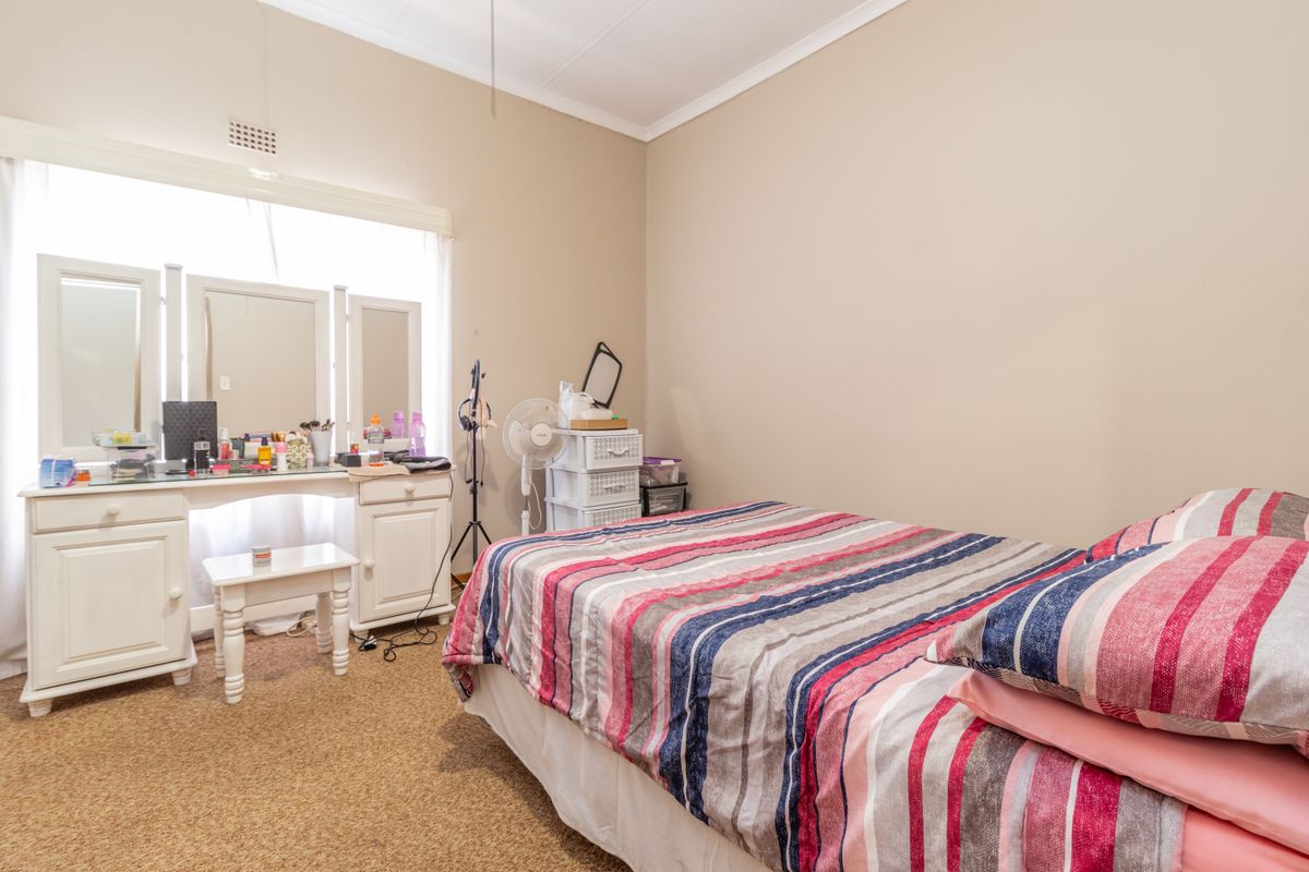 A bedroom featuring beige walls, carpeted flooring, and a large window with natural light.