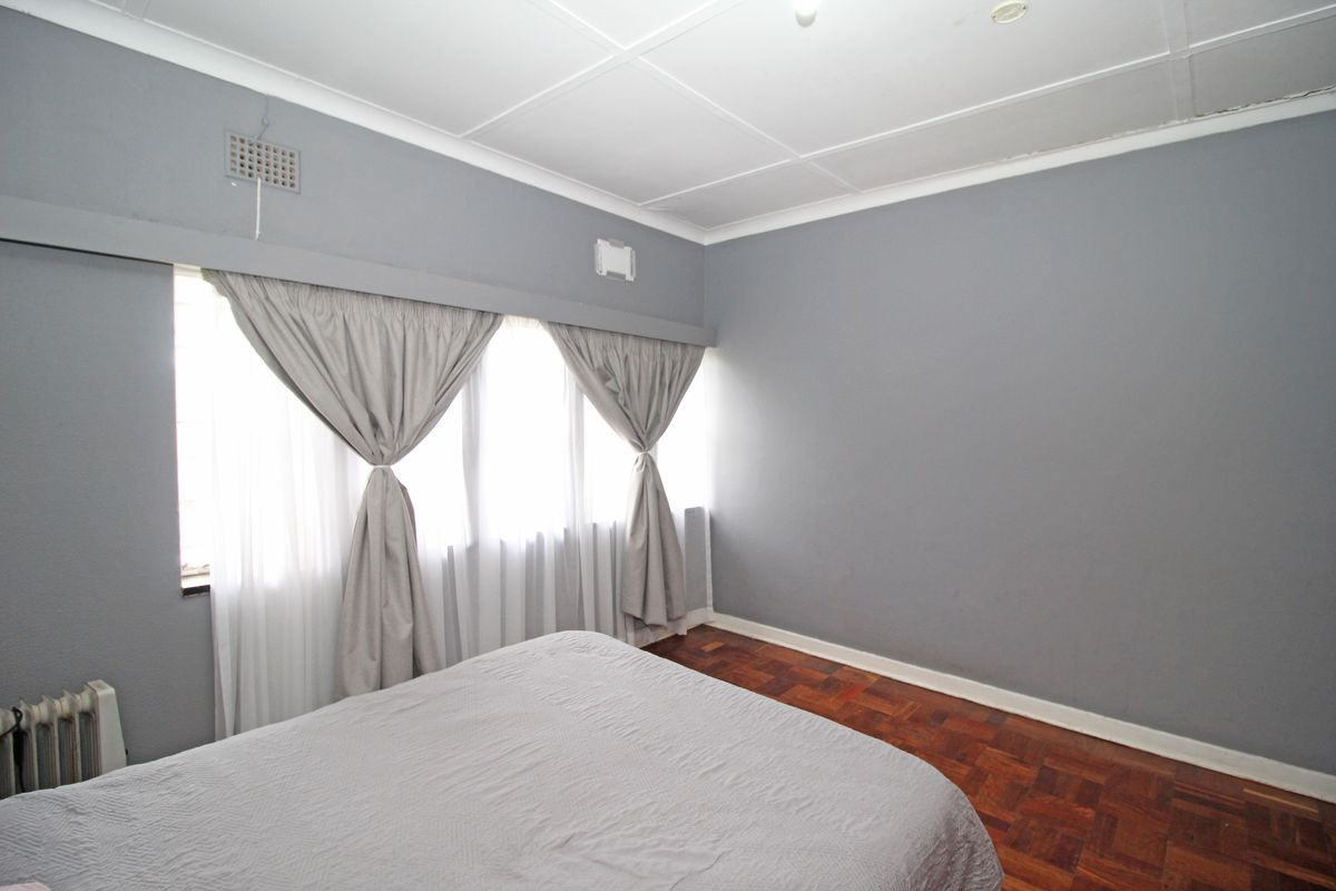 A bedroom featuring parquet flooring, grey painted walls, and large windows with curtains, providing a neutral space ready for personalization.