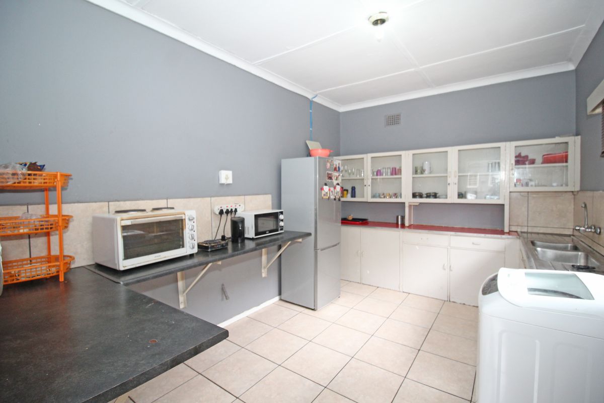 Functional kitchen featuring tiled flooring, built-in cabinetry with glass-fronted upper cupboards, laminate countertops, and a double stainless steel sink.