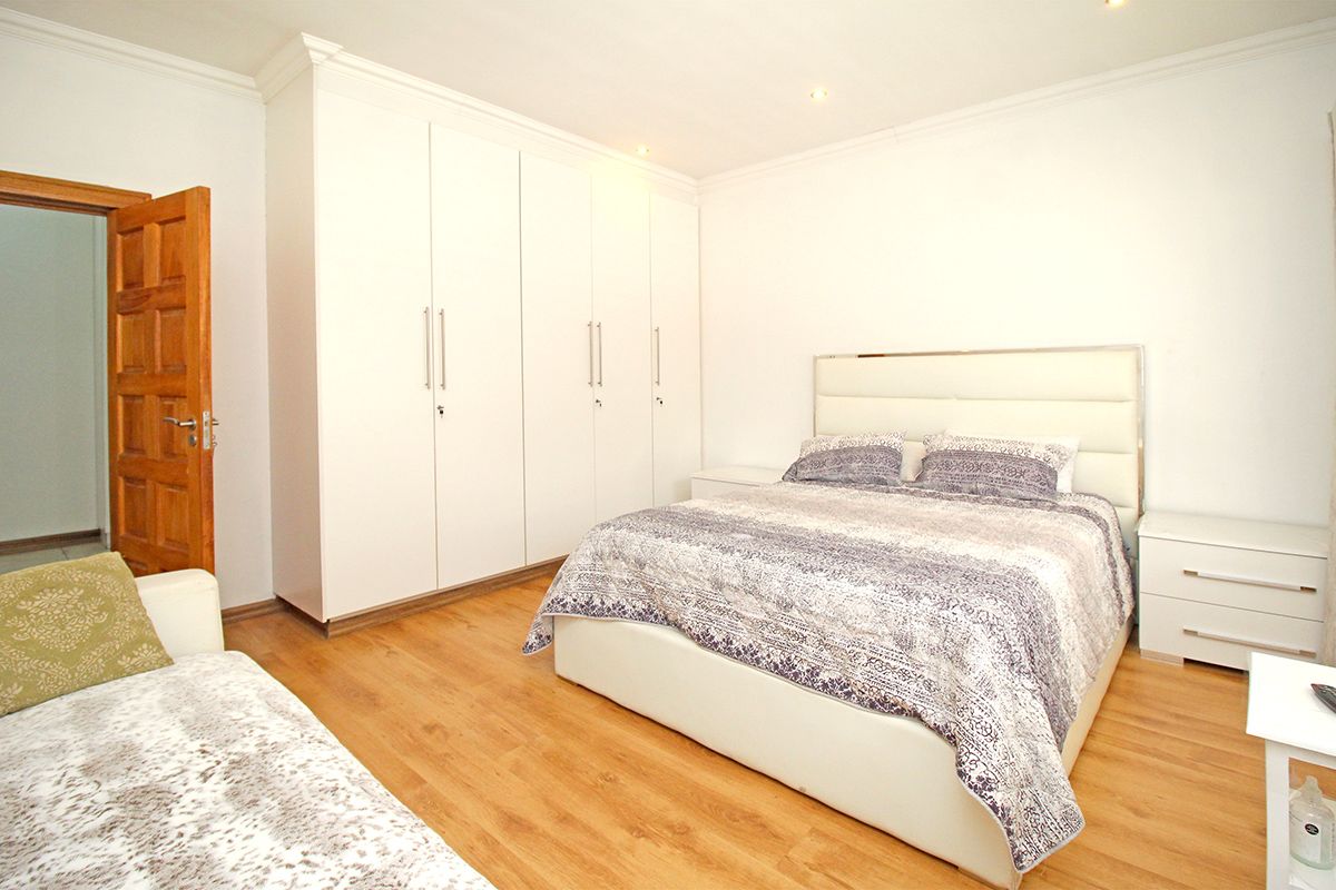 A well-maintained bedroom featuring built-in floor-to-ceiling wardrobes, laminate wood flooring, and recessed ceiling lighting.