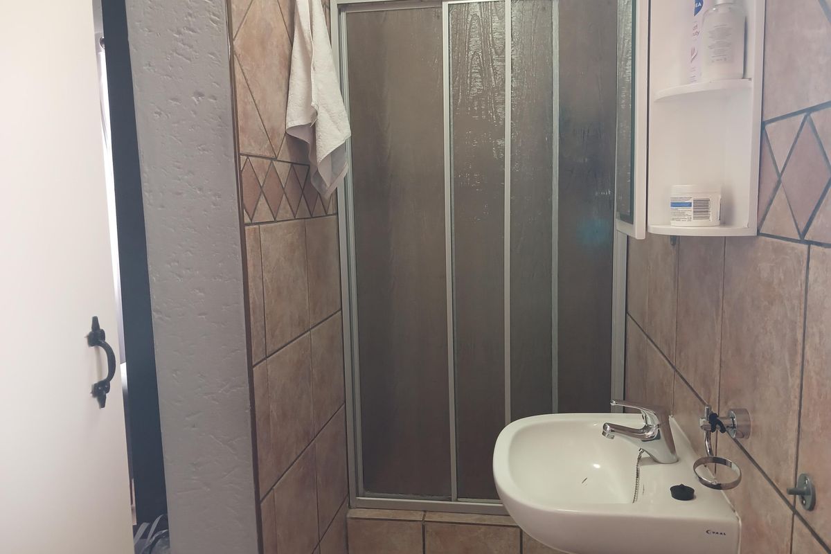 A compact bathroom featuring a pedestal basin, tiled walls, and a framed shower enclosure.