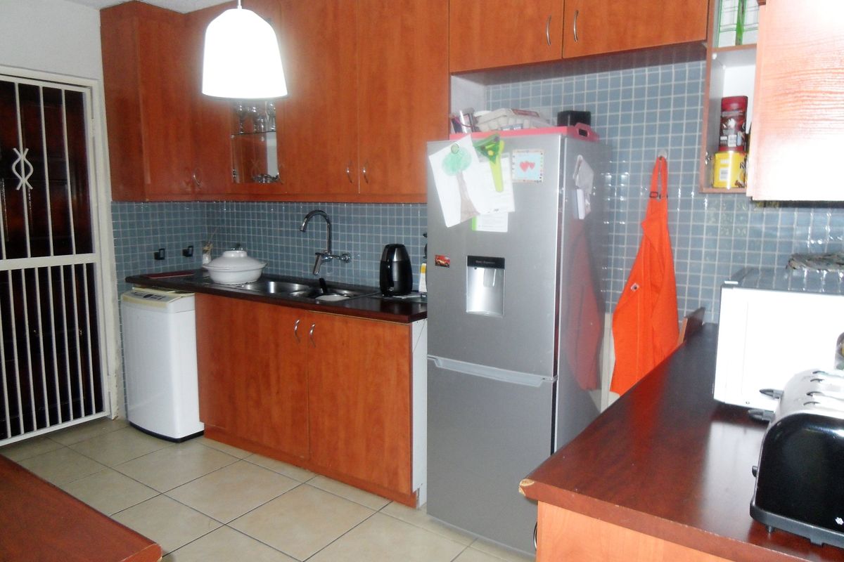 Functional kitchen featuring wood-look cabinetry, tiled backsplash, double sink, and tiled flooring, with direct access to an exterior security door.