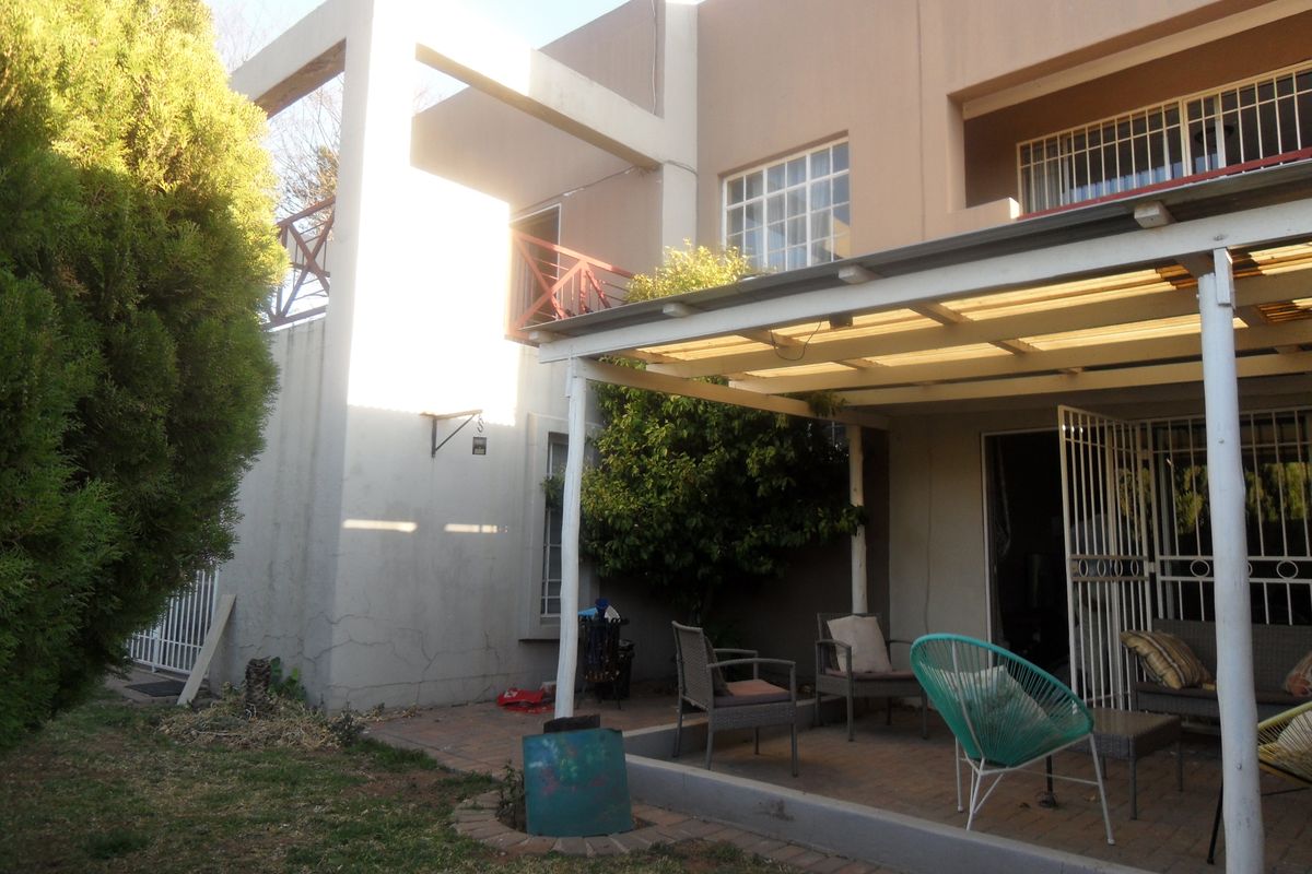 Rear view of the townhouse featuring a paved patio area with a covered pergola and an upper-level balcony with metal railings.