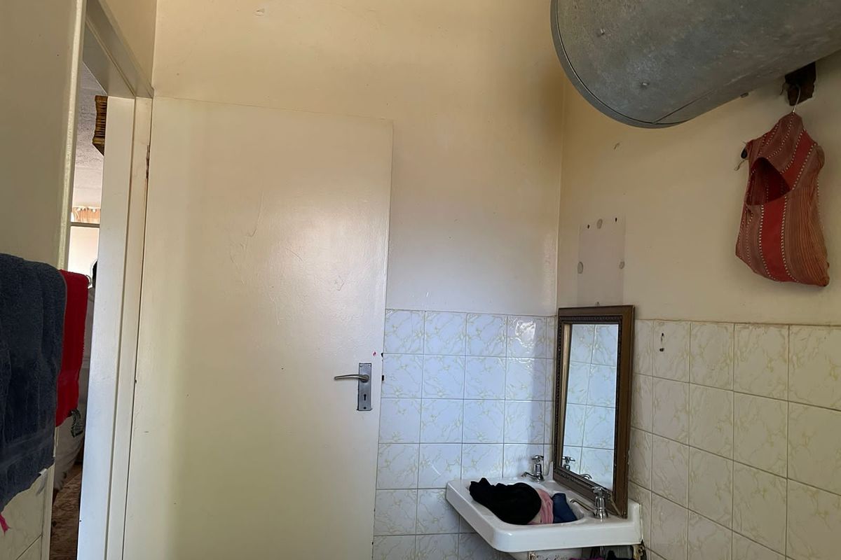 A small bathroom area featuring a wall-mounted basin, tiled splashback, and an exposed water heater tank.
