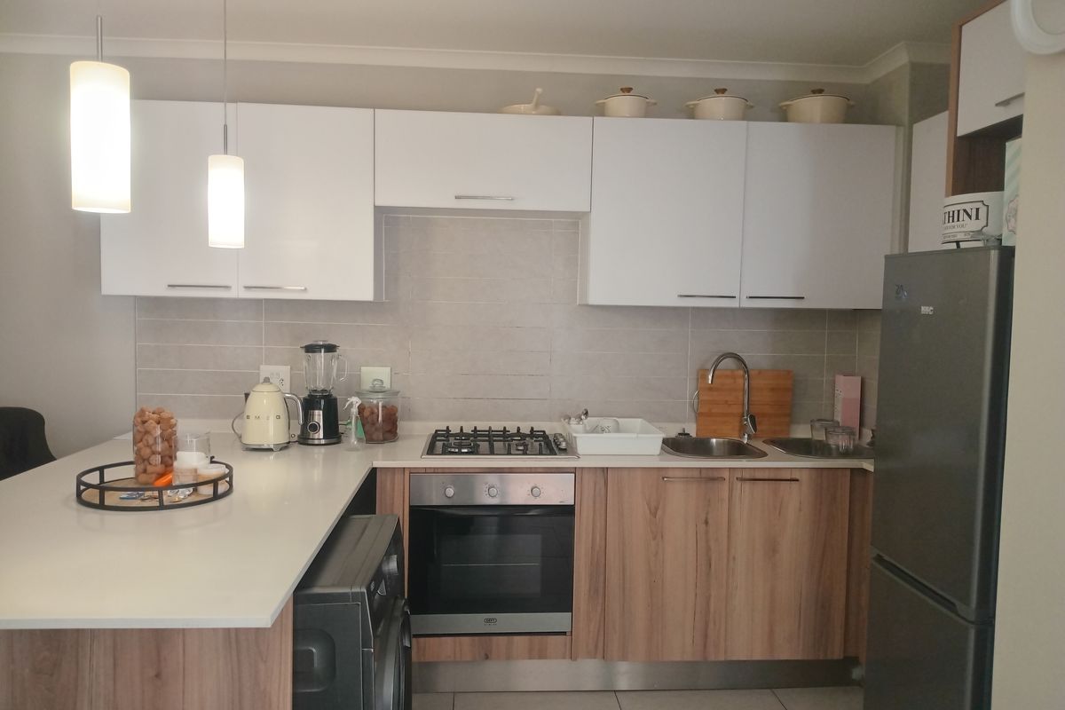 Modern kitchen featuring white upper cabinetry, wood-finish lower cabinets, stone countertops, a built-in gas hob, oven, and integrated sink area.