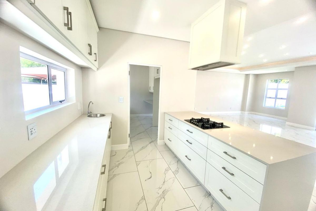 Modern kitchen featuring white cabinetry, stone countertops, a central island with a built-in gas hob, and marble-look floor tiles, leading into an open-plan living area.
