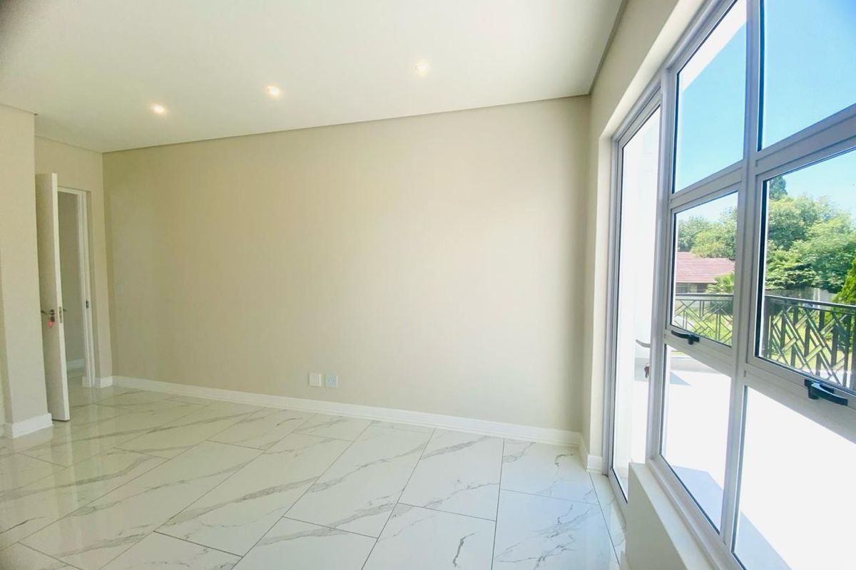 A bright, empty living room featuring modern marble-look floor tiles, recessed ceiling lighting, and large glass sliding doors leading to an outdoor balcony.
