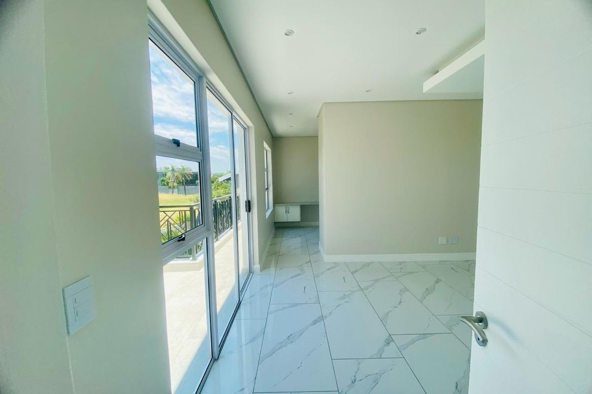 A bright, modern bedroom featuring large sliding glass doors leading to a balcony, marble-look floor tiles, and recessed ceiling lighting.
