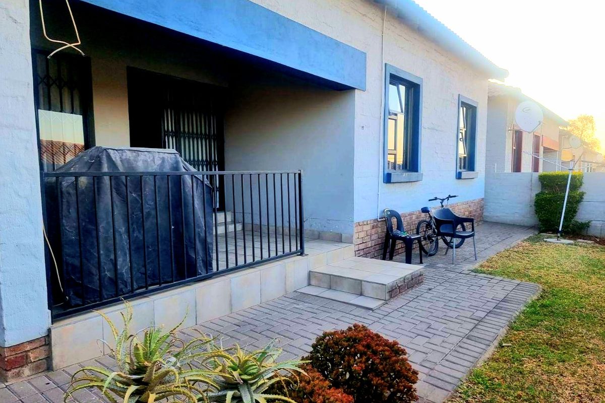 A view of the rear exterior featuring a paved patio area, metal security gate, and a covered porch space.