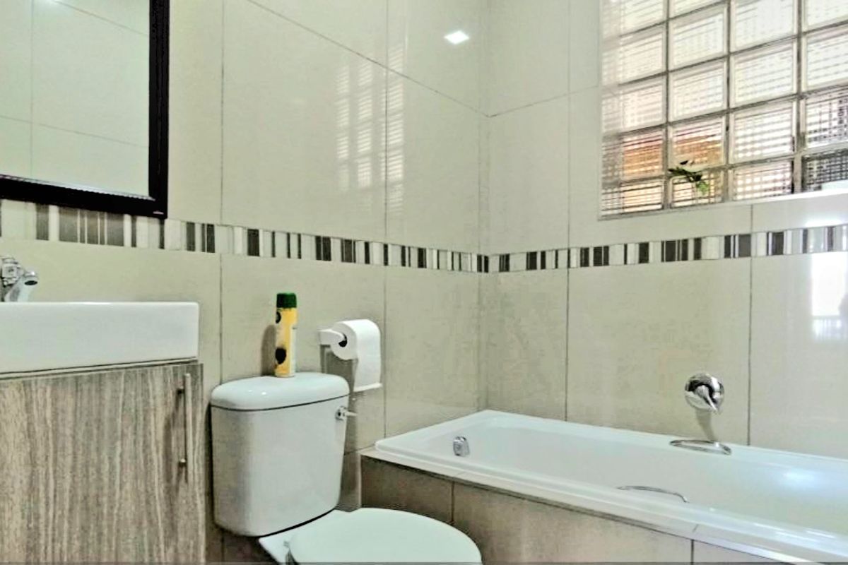A functional bathroom featuring a built-in bathtub, a wall-mounted vanity with a basin, and a glass block window for natural light.