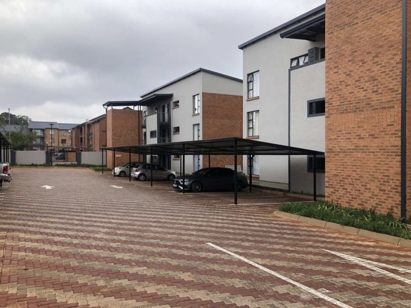 Exterior view of a modern apartment complex featuring brick and rendered facades, paved parking areas, and covered parking bays.