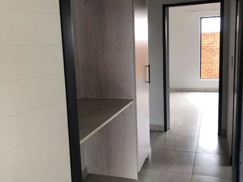 A modern hallway featuring tiled flooring, exposed concrete ceilings, and built-in cabinetry, leading into an adjacent room with natural light.