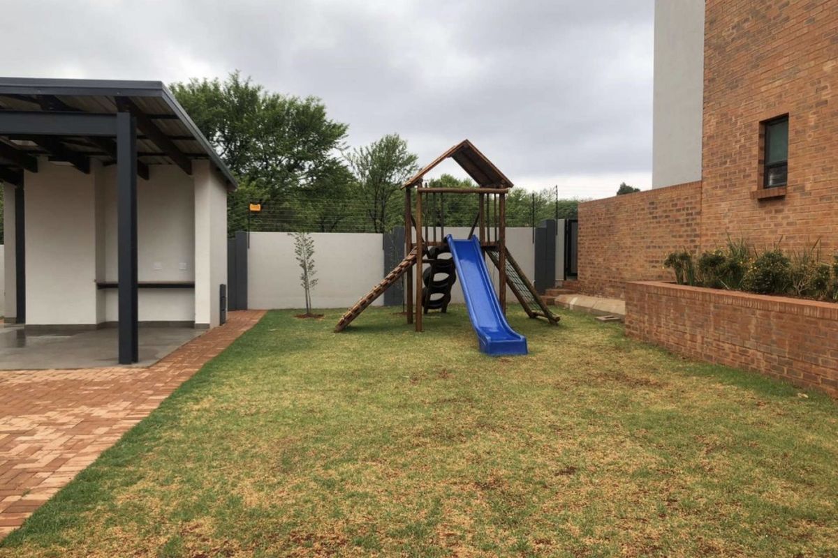 A private rear garden featuring a covered patio area, brick paving, and a lawn with a built-in play structure.