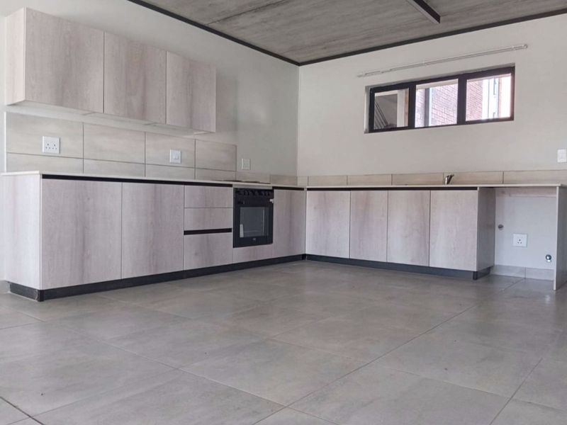 Modern kitchen featuring light wood-grain cabinetry, built-in oven, tiled flooring, and an exposed concrete ceiling in an open-plan layout.
