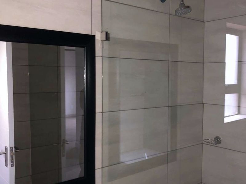 A modern bathroom featuring large format wall tiles, a glass shower enclosure, and a contemporary basin mixer tap.