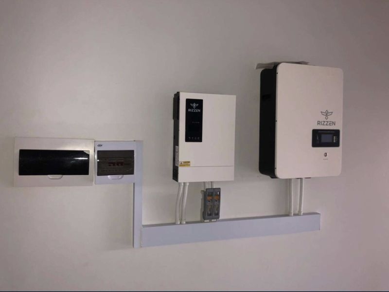 A clean installation of a solar power inverter and battery management system with associated electrical distribution boards mounted on a wall.
