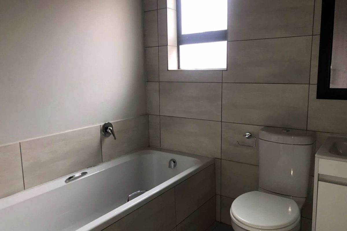 A clean, modern bathroom featuring a built-in bathtub, a toilet, and a vanity unit with neutral wall and floor tiling.